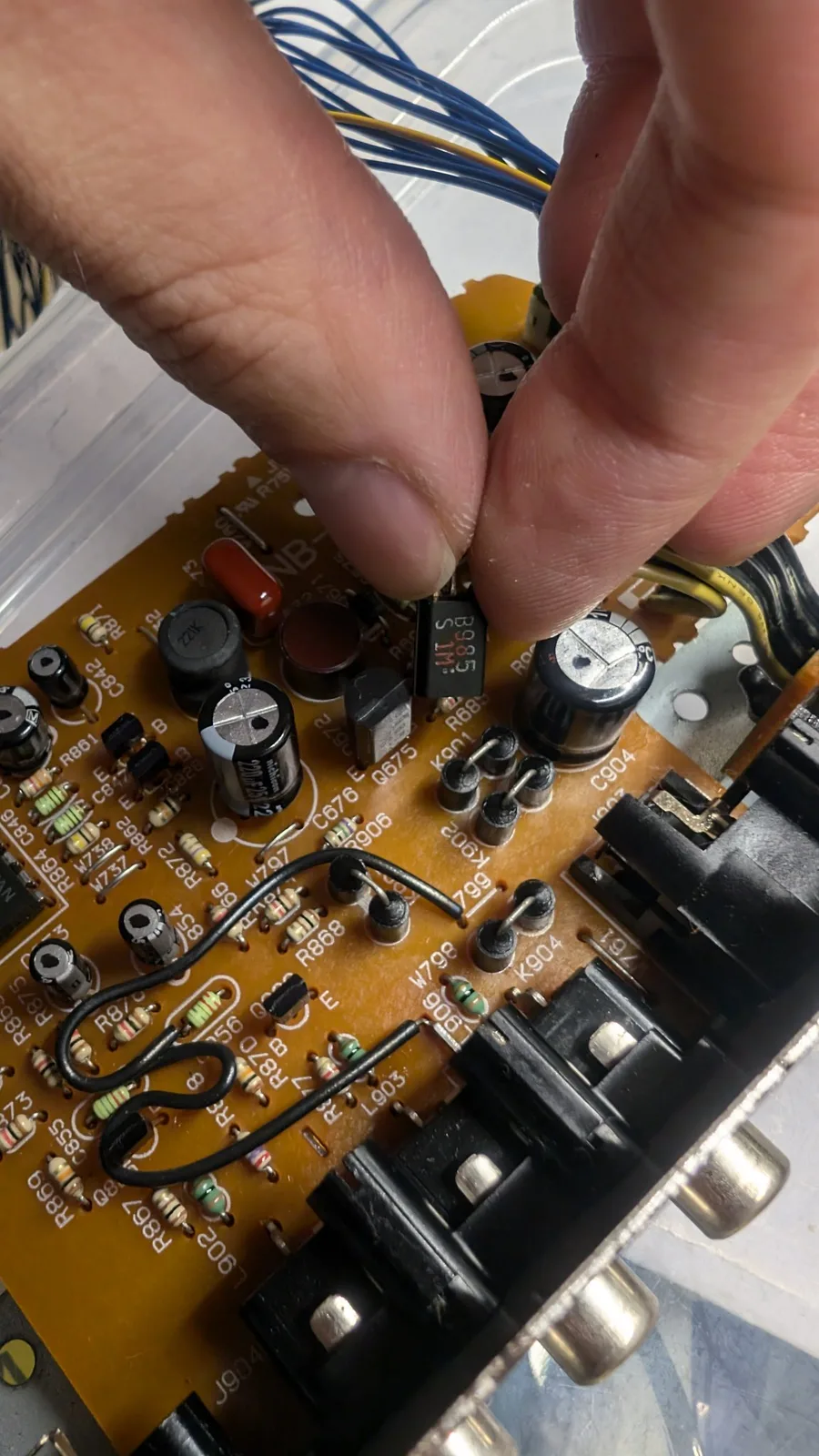Hands holding tweezers over Wondermega AV board, replacing transistor and DC-DC converter among various resistors and capacitors.