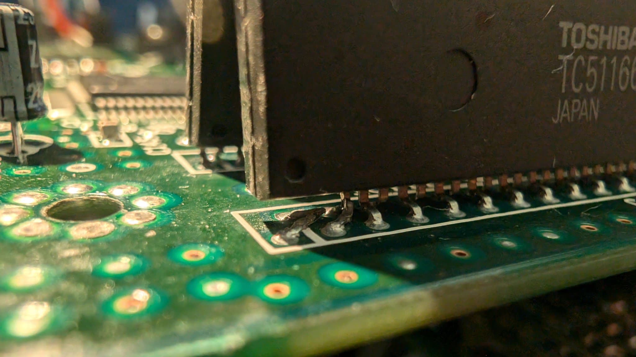 Close-up of Wondermega MCB showing damaged RAM package with broken legs next to IC chip, green PCB with solder joints and copper pads visible.