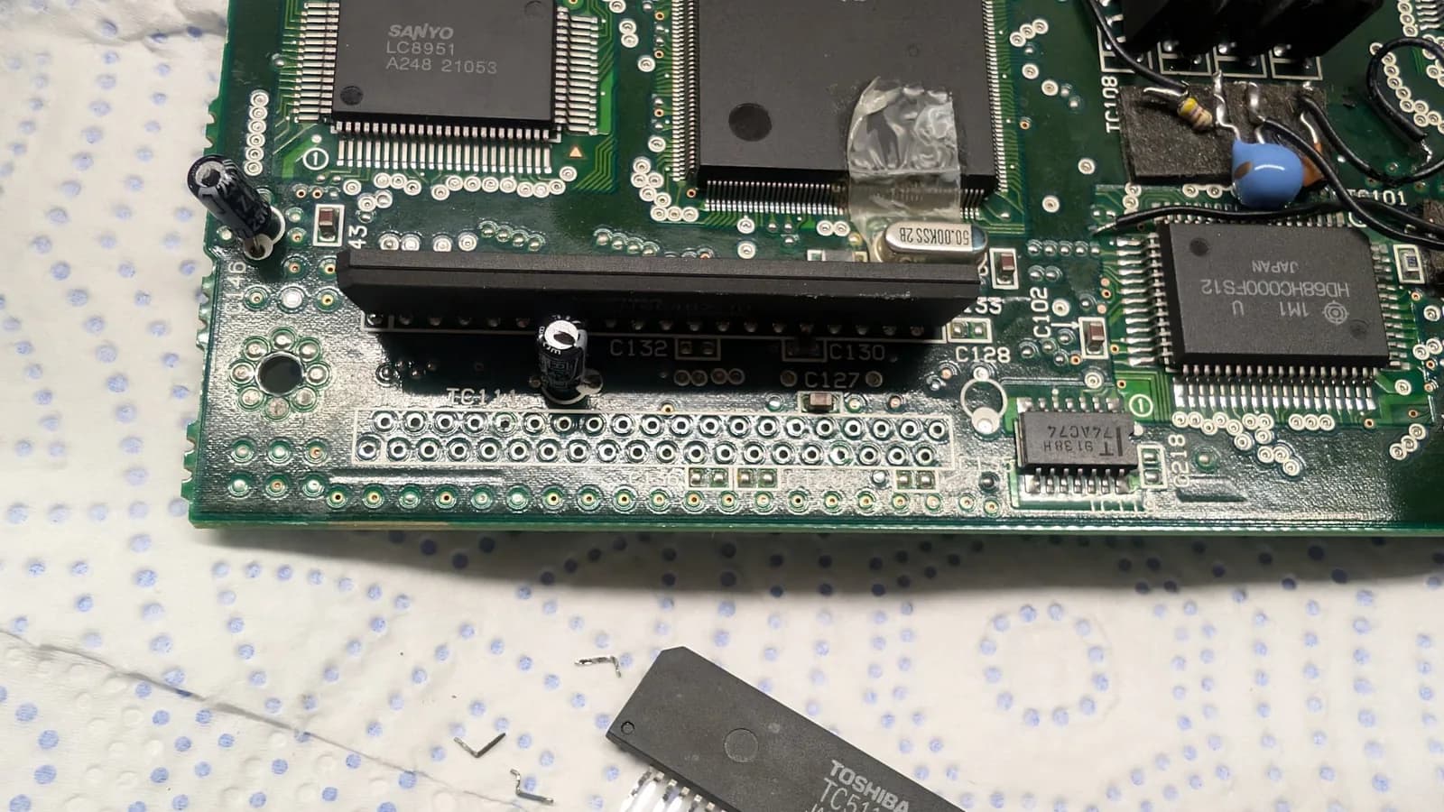 Extracted RAM chip with three broken legs displayed below Wondermega motherboard during repair documentation.