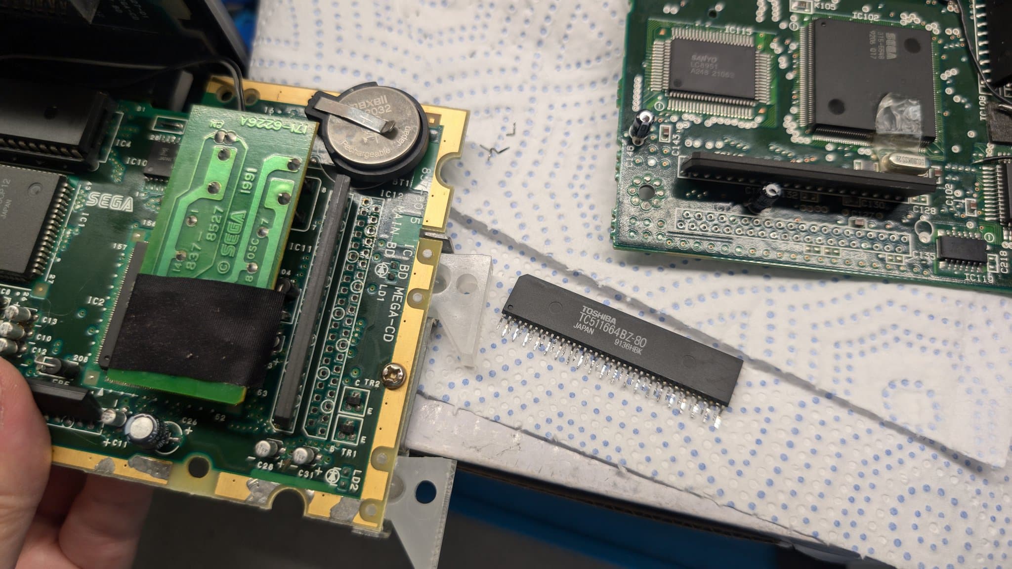 Extracted RAM package from donor MCD1 board held next to Wondermega motherboard during reinstallation troubleshooting.
