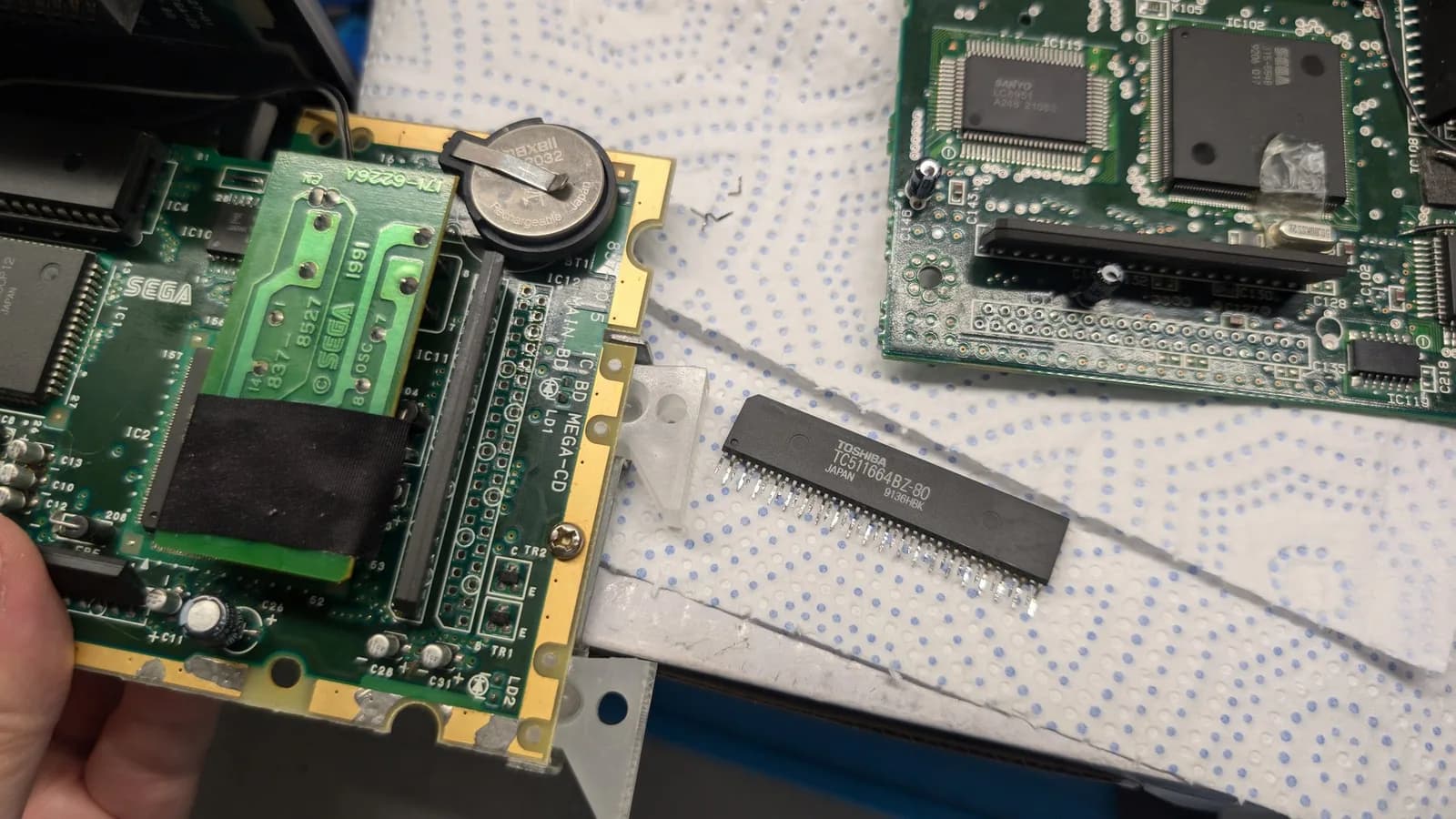 Extracted RAM package from donor MCD1 board held next to Wondermega motherboard during reinstallation troubleshooting.
