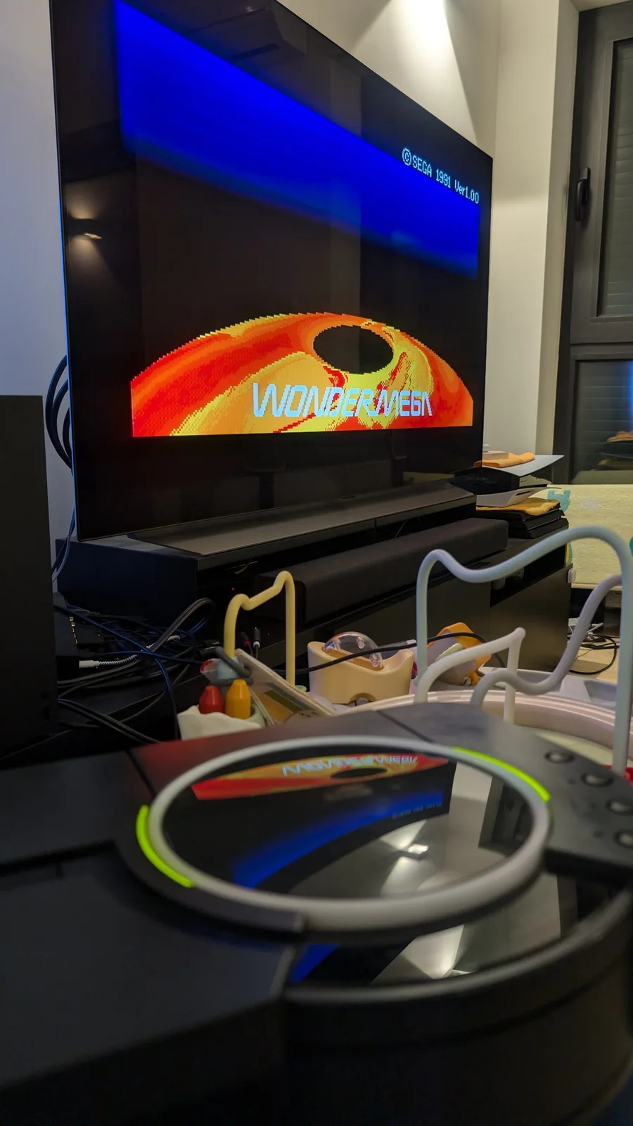 Sega Wondermega displaying 240p test suite on TV; steering wheel controller in foreground; repair workspace with tools and components visible.