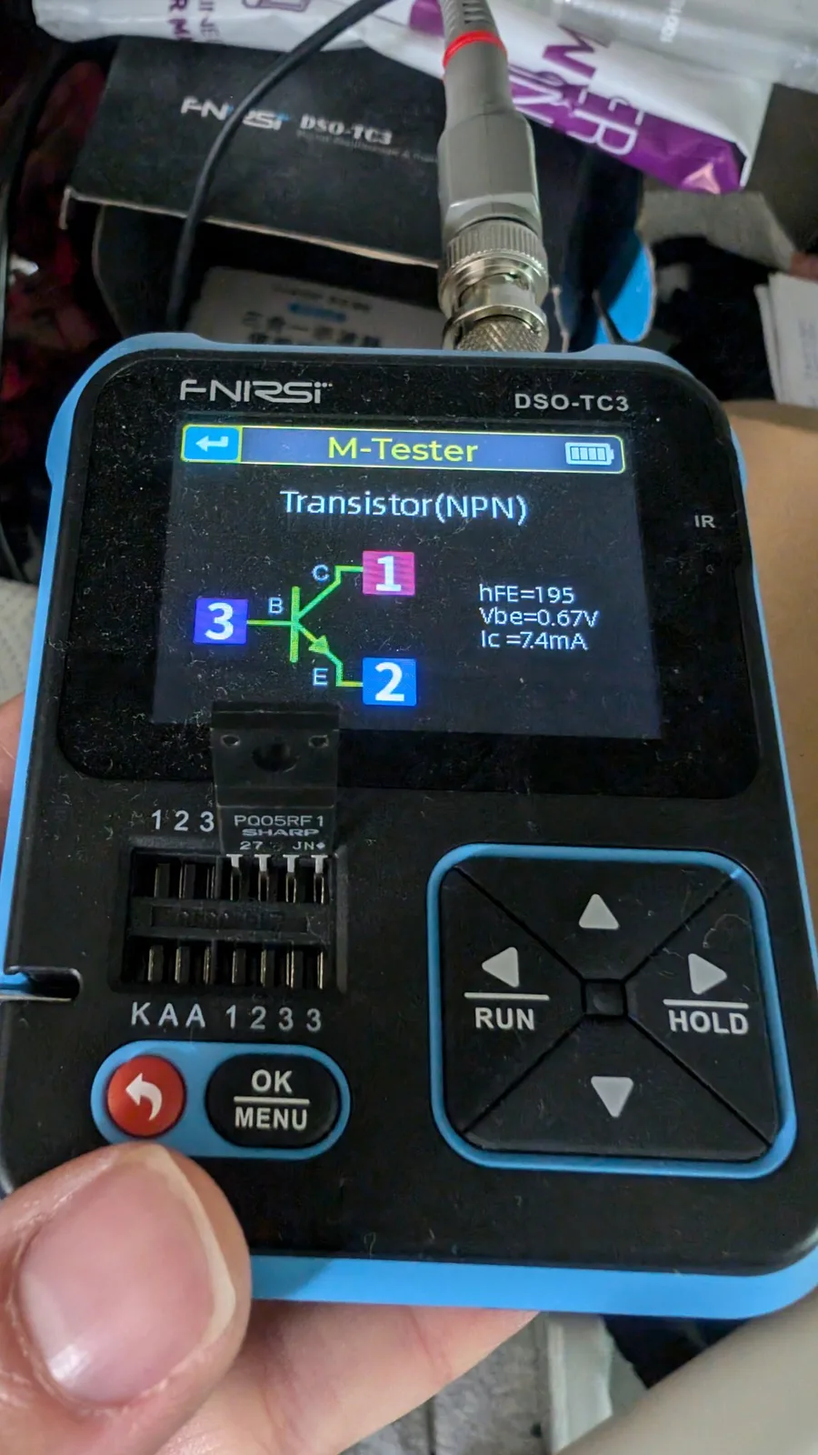 FNIRSI DSO-TC3 multimeter displaying NPN transistor test results: hFE=195, Vbe=0.67V, Ic=7.4mA with probe connected.