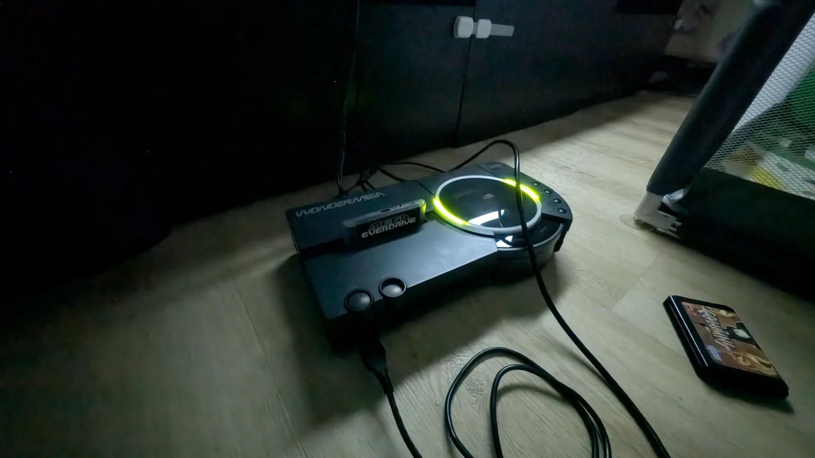 Sega Wondermega with Mega ED Pro cartridge displaying yellow LED, connected to smartphone showing game footage on wooden desk.