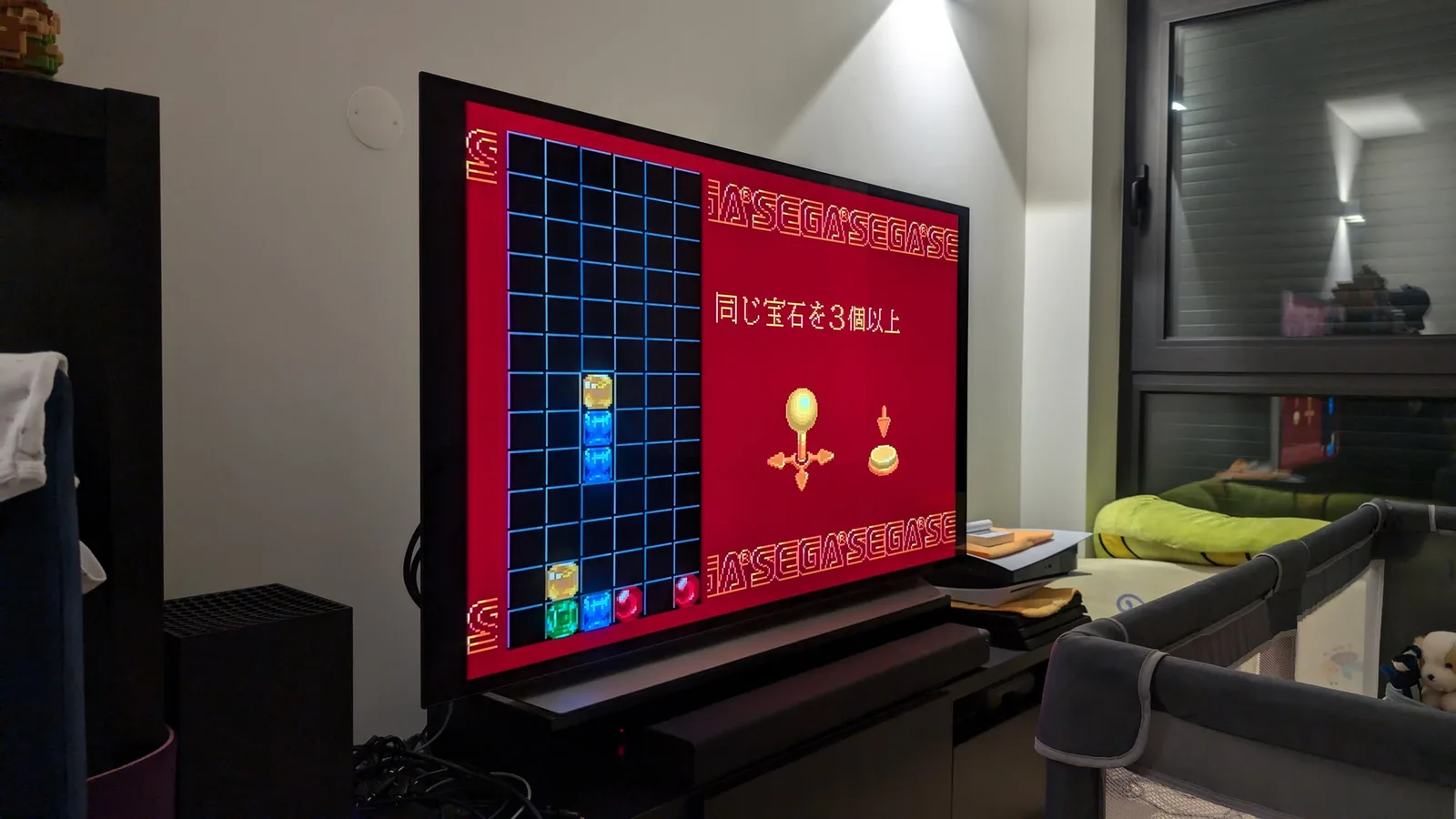 Sega Wondermega displaying Mega Drive game with colorful gem-matching puzzle on red background, connected controllers visible.