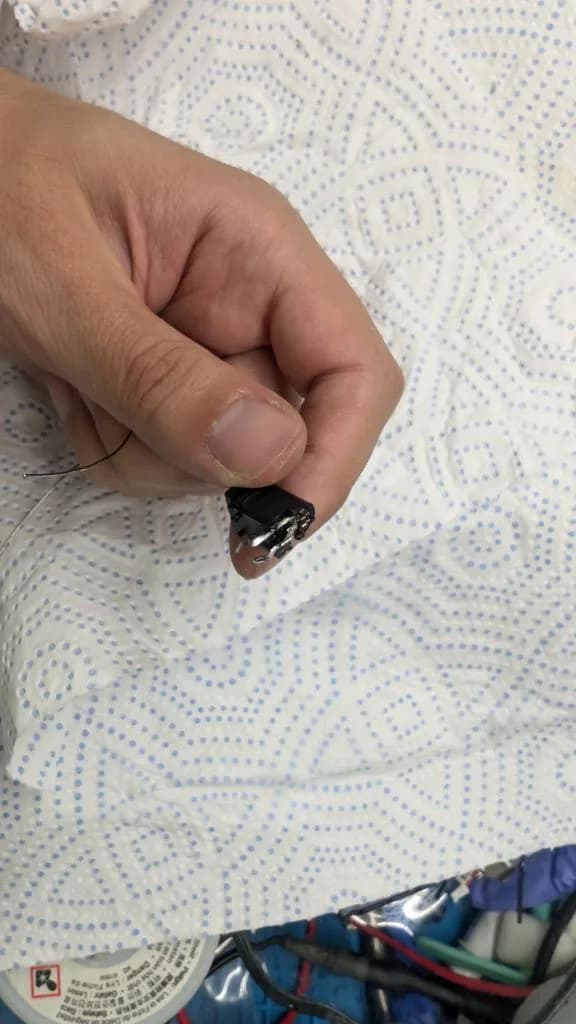 Close-up of tinned regulator legs being held with tweezers over patterned fabric during Wondermega restoration work.