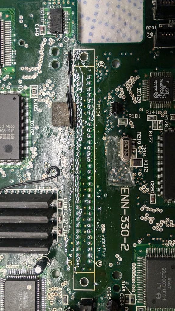 Sega ENN-530-2 PCB with corroded cartridge connector area; fiberglass pen scraping visible on traces near via points.