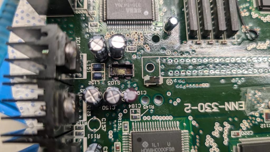 Sega Wondermega motherboard with cartridge connector area exposed, showing corrosion and fiberglass pen scraping work on detection button contacts.
