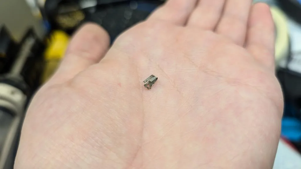Small electronic component held in palm of hand during Wondermega repair, showing scale of tiny circuitry work.