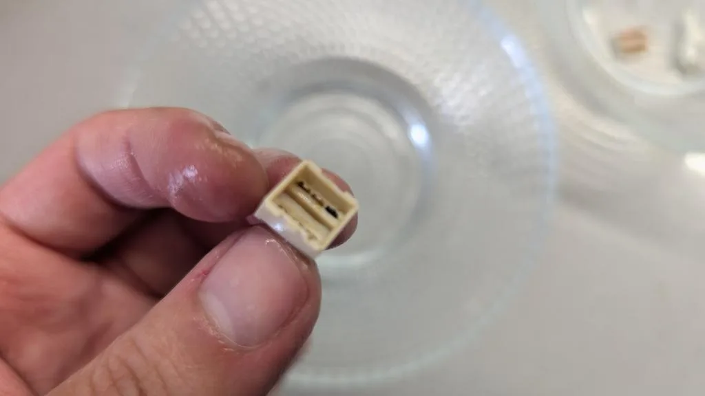 Corroded desoldered power button component held in tweezers, showing oxidized metal contacts and deterioration from the Wondermega restoration.
