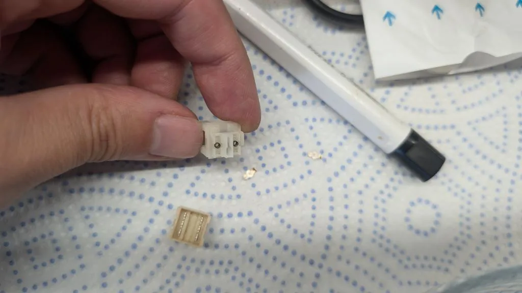 Desoldered power and reset button switches showing corrosion on contacts, held over blue dot patterned work mat with desoldering tools nearby.