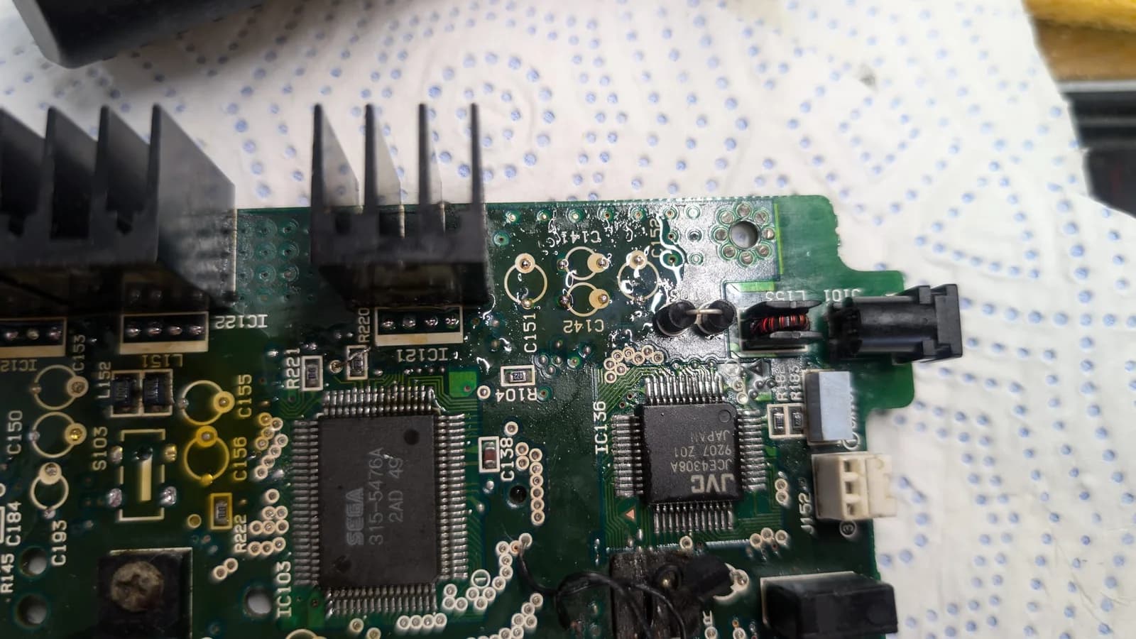 Sega Wondermega PCB with solder flooding technique applied to through holes; black solder wick visible above board during water damage restoration.