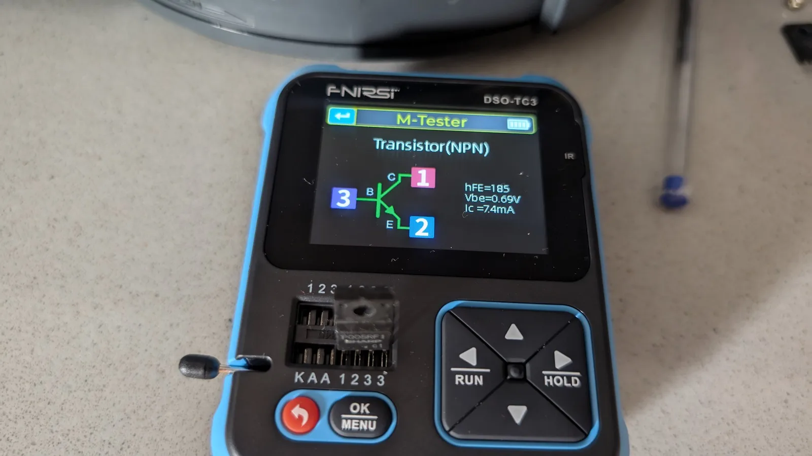 FNirsi DSO-TC3 multimeter displaying NPN transistor test results: hFE=105, Vbe=0.69V, IC=7.4mA during Wondermega regulator testing.