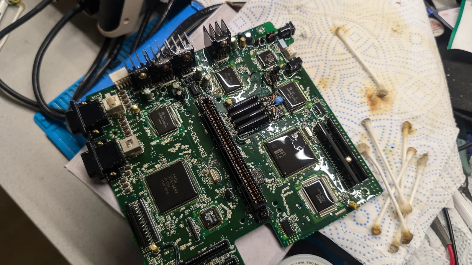 Cleaned Wondermega main board on blue mat with isopropyl residue visible; multiple ICs and connectors exposed after corrosion removal.