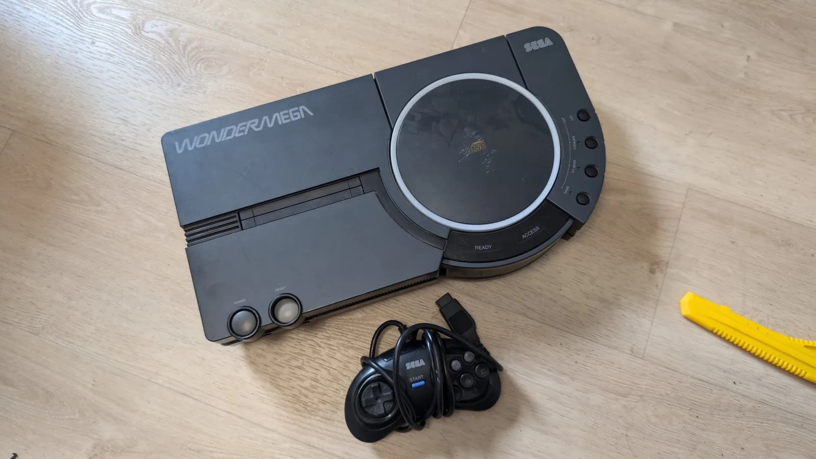 Sega Wondermega console with controller and yellow tool on wooden surface, showing unit awaiting repair.