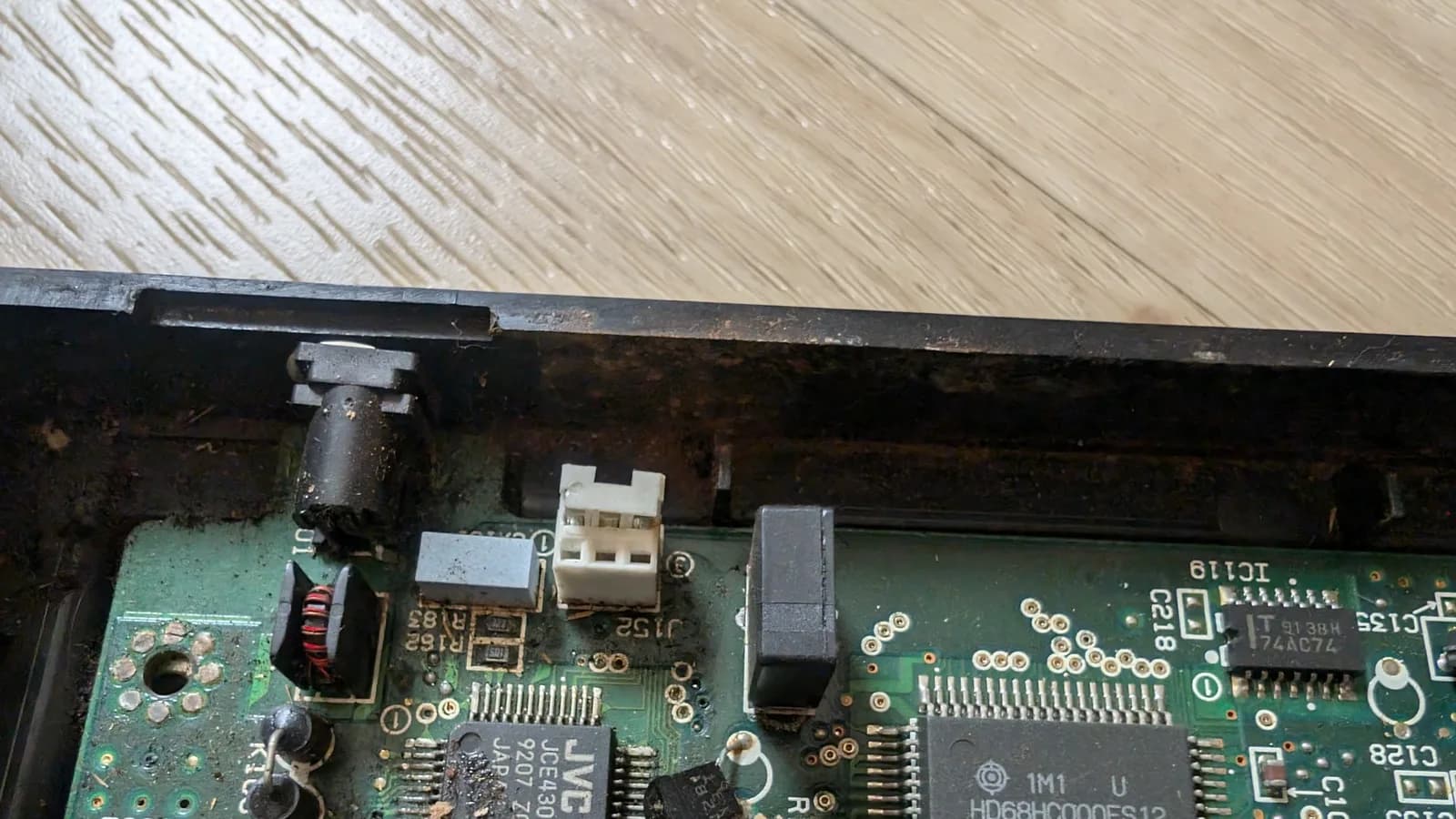 Corroded Wondermega circuit board with oxidized components, broken connector, and damaged traces visible under work light during restoration.