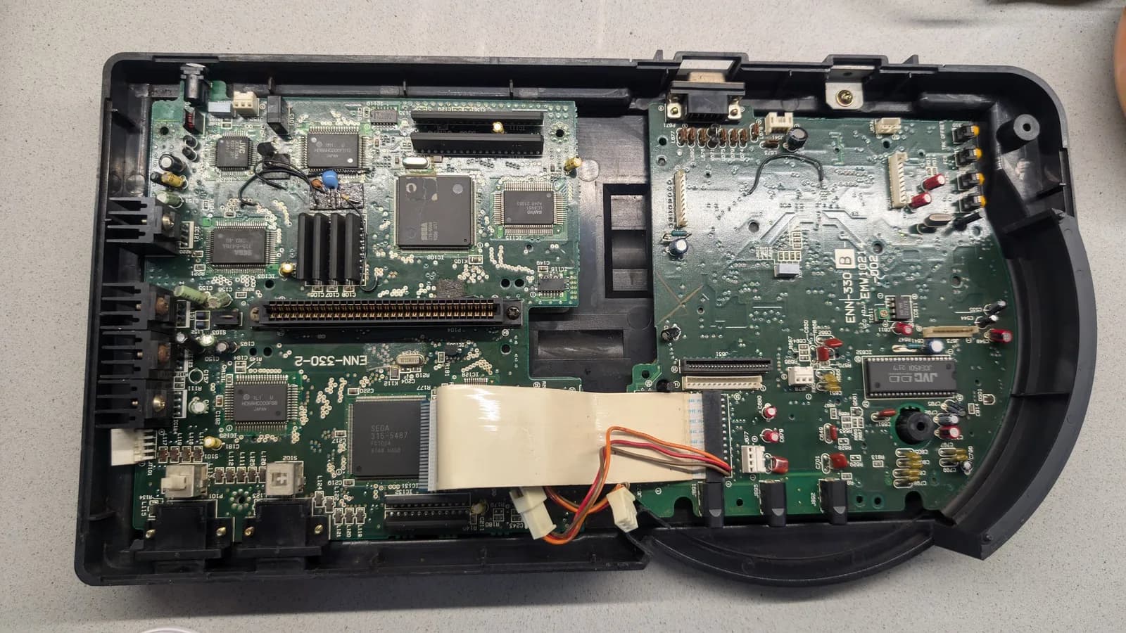 Wondermega main PCB after cleanup showing corrosion damage, faded regulator component, possible broken trace, and intact lower board section.