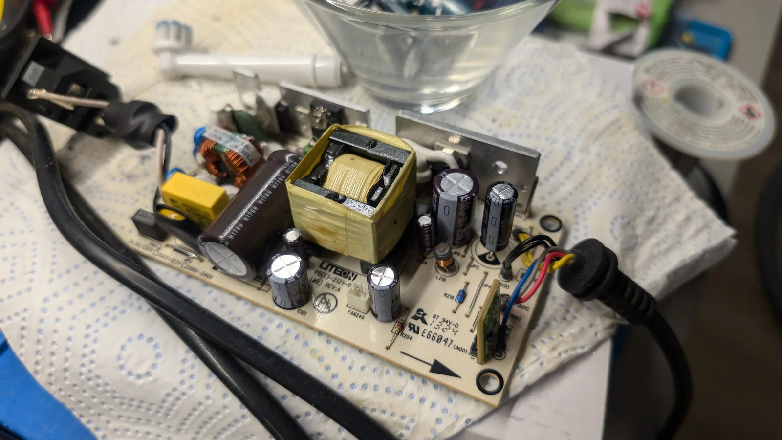 Xbox 360 E PSU board with replaced Nichicon capacitors, transformer, and cleaned components on work surface during recapping maintenance.