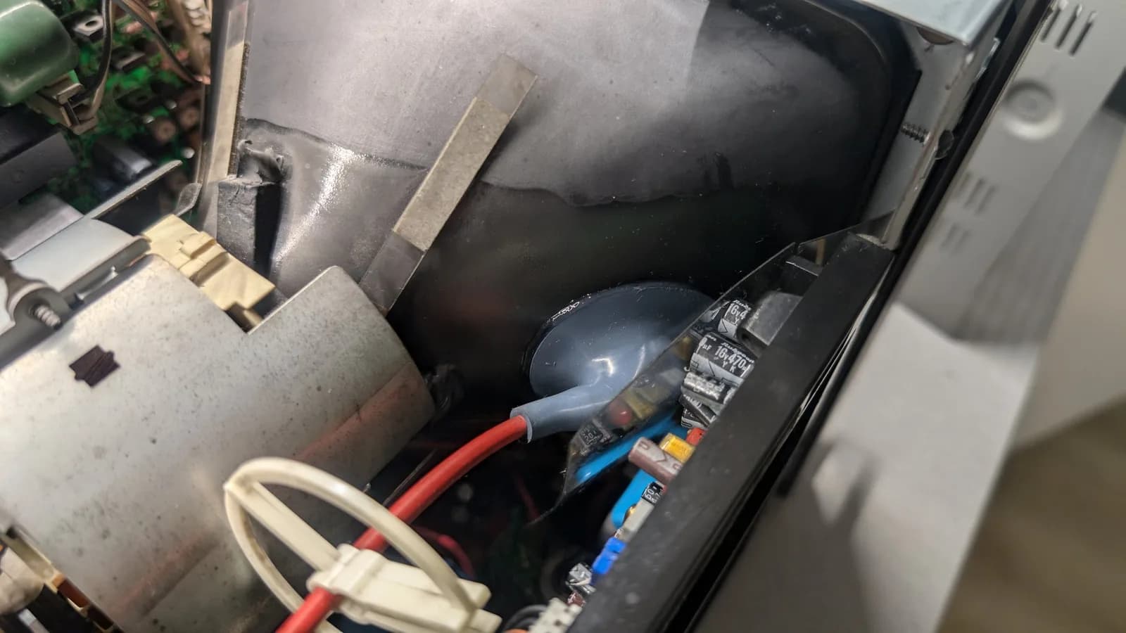 Inside the Sony PVM-9045QD at the CRT anode connection, the red high-voltage lead entering the grey rubber anode cap (repacked with dielectric grease), with electrolytic capacitors and cable-tied wiring alongside.