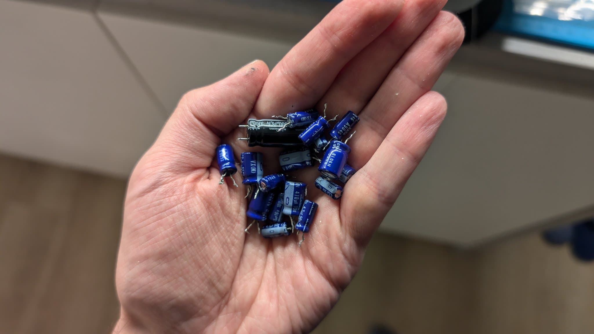 A hand holding the blue electrolytic capacitors removed during the partial mainboard recap, including one black capacitor among them.