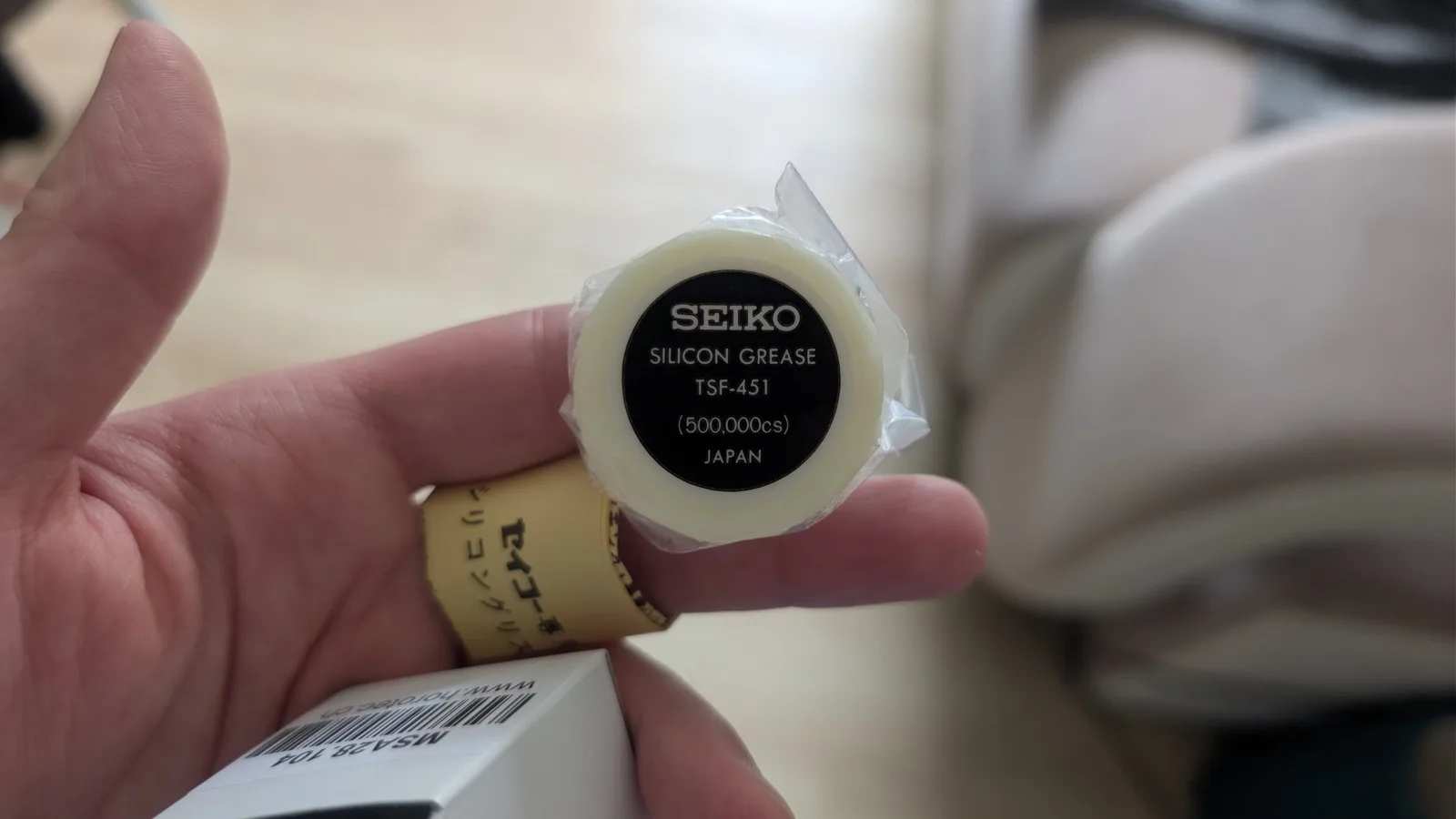 Hand holding Seiko Silicon Grease TSF-451 container, 500,000cs viscosity, made in Japan for watch repair work.
