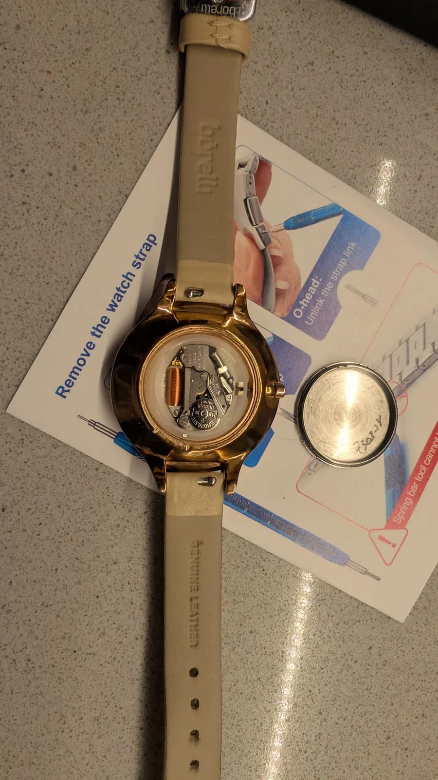 Disassembled watch with caseback removed, showing internal mechanism with balance wheel visible; repair tools and instruction manual laid beside it.
