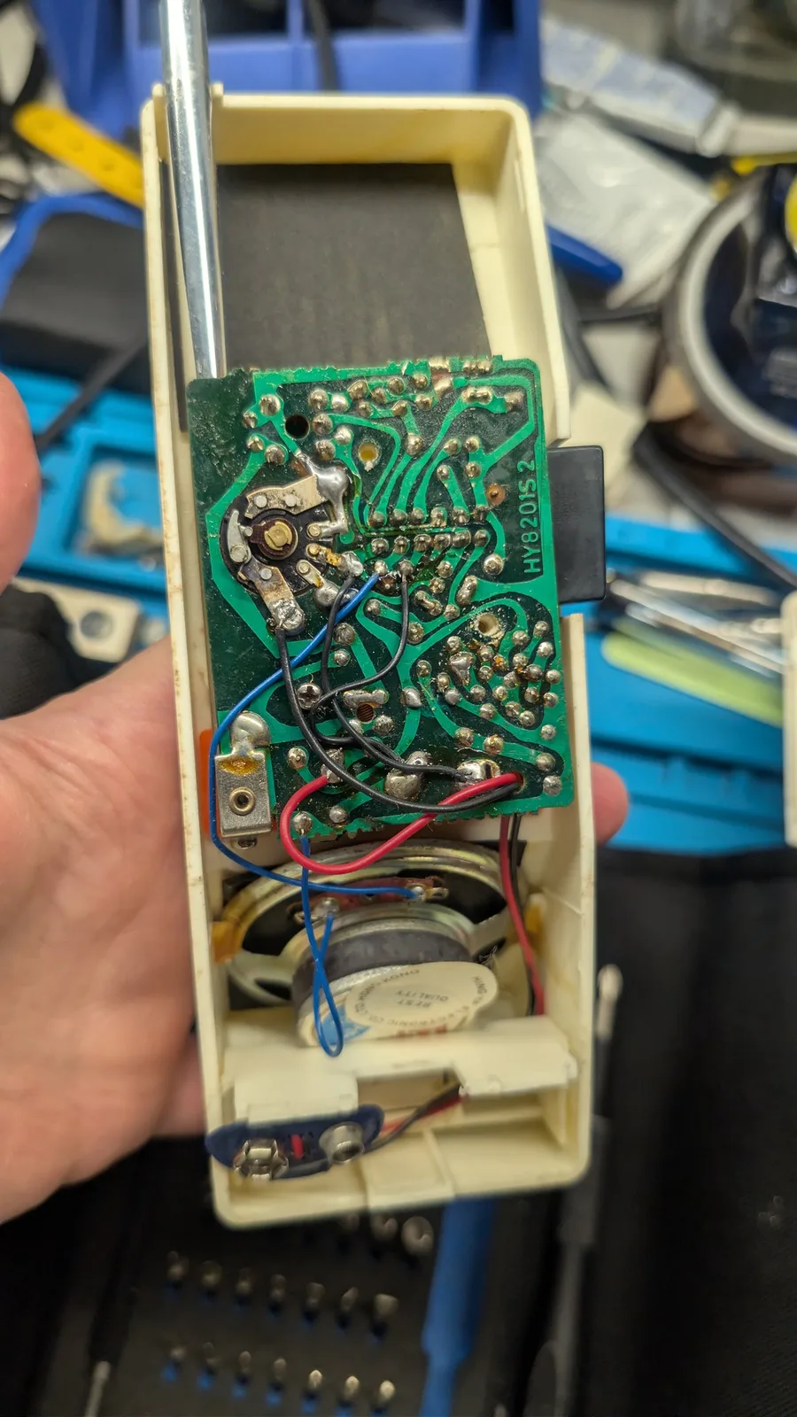 Green PCB with electrolytic capacitor, potentiometer, and colored wires in cream plastic walkie-talkie housing during refurbishment.