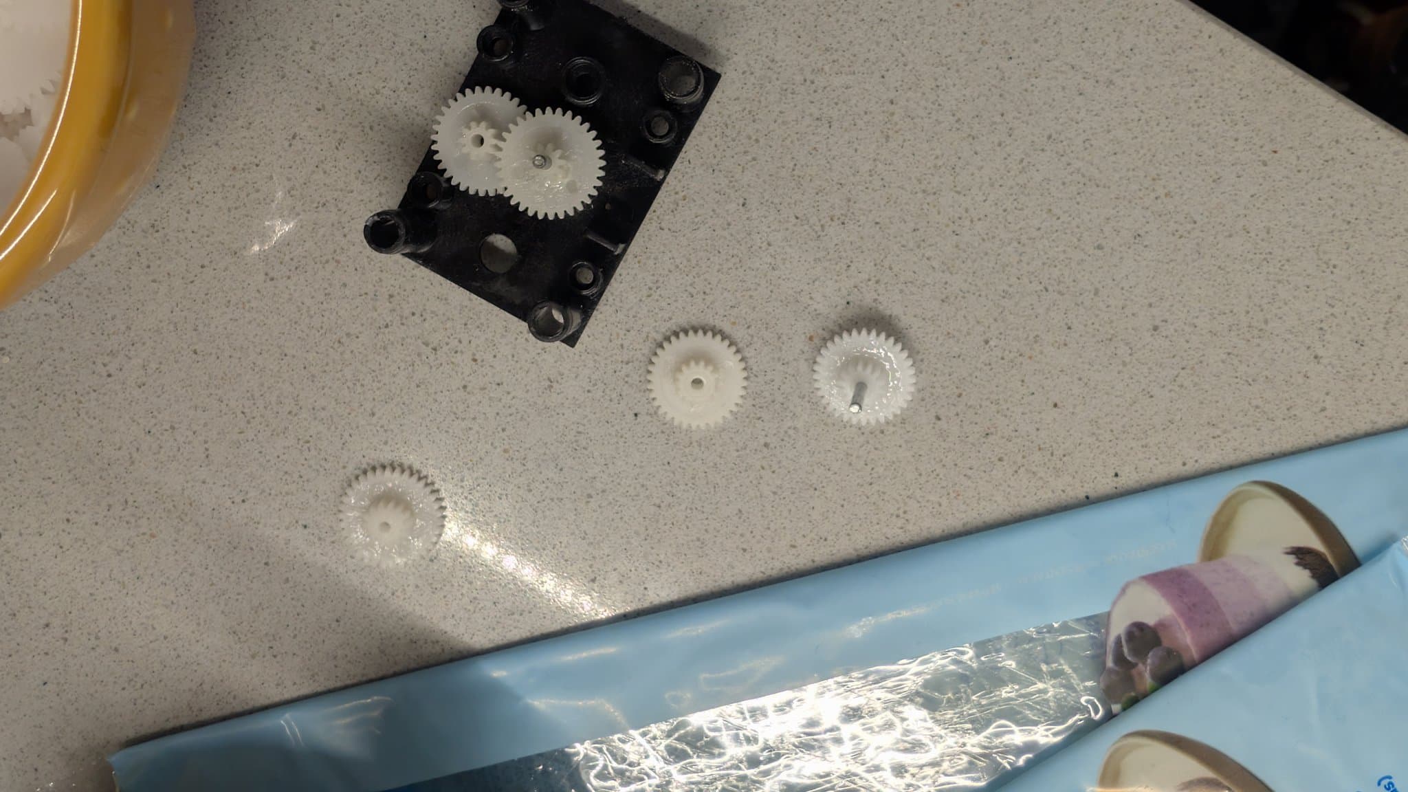 Black gear housing with two meshed gears on top; three individual plastic gears below showing filing marks; repair components for Totoro toy motion mechanism.