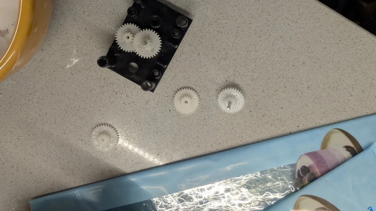 Black gear housing with two meshed gears on top; three individual plastic gears below showing filing marks; repair components for Totoro toy motion mechanism.