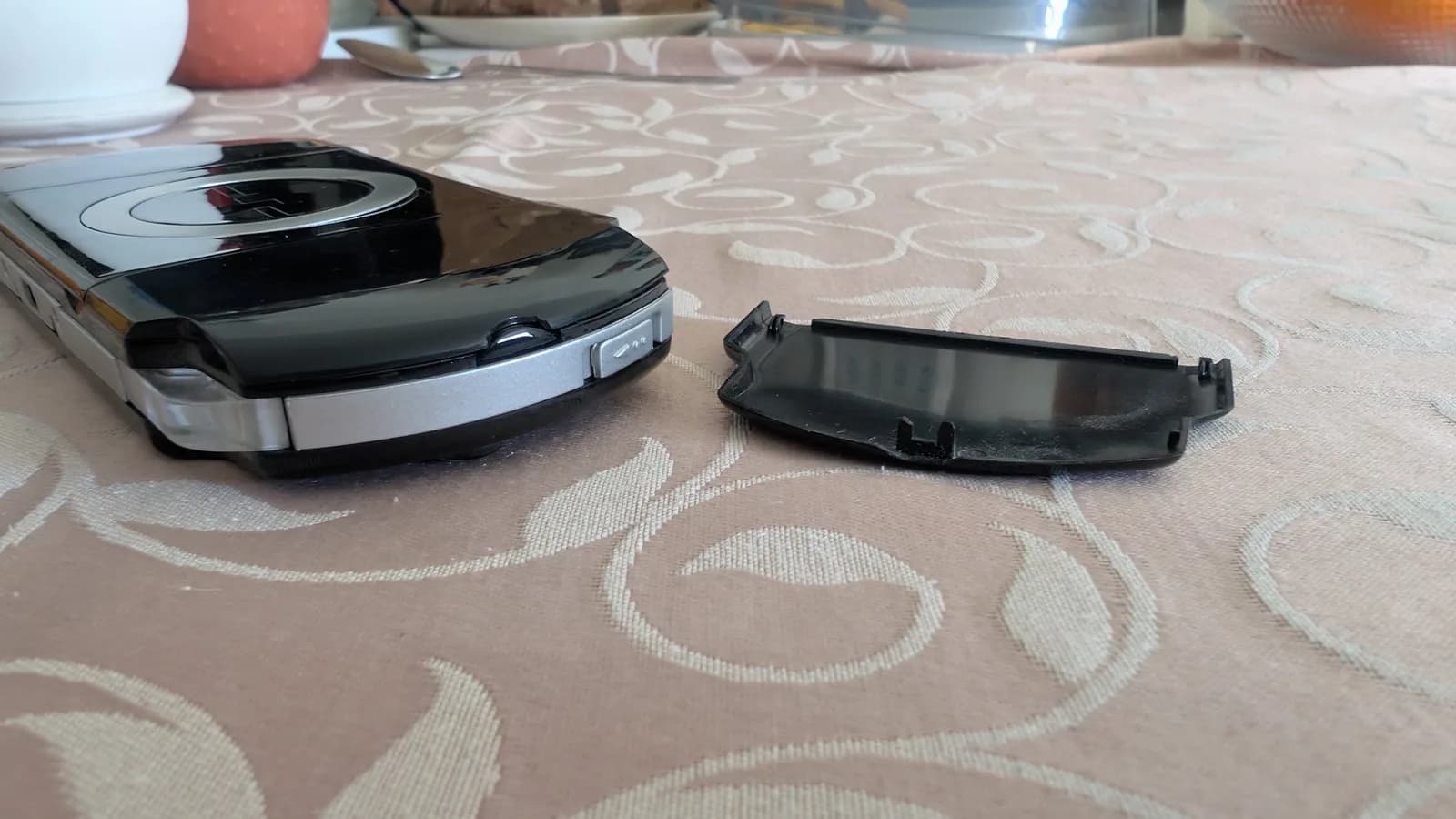 Swollen PSP battery next to broken battery door with damaged retaining clip on patterned fabric surface.