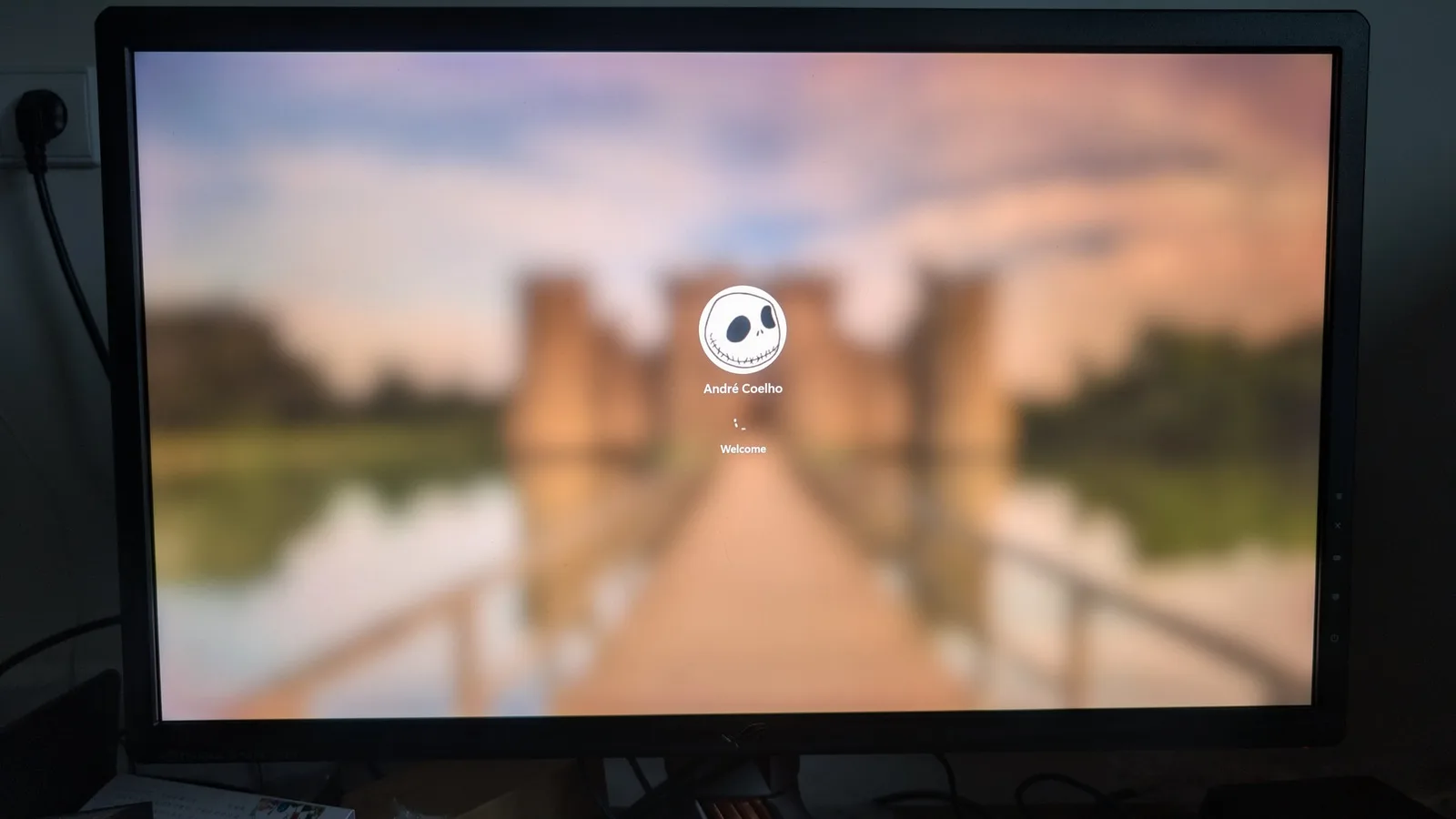 Asus PG27UQ monitor displaying boot screen with "André Coelho" user profile and "Welcome" text during post-repair startup verification.