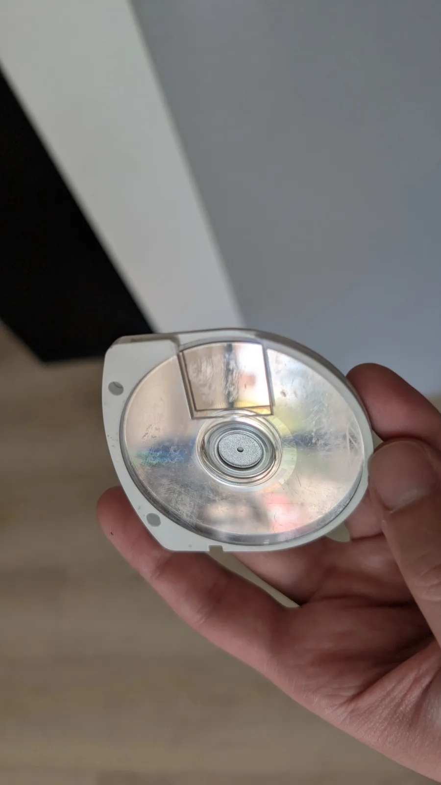 The reflective data side of the Gran Turismo UMD in its white cartridge shell, held in hand, the mirrored surface dirty and smudged.