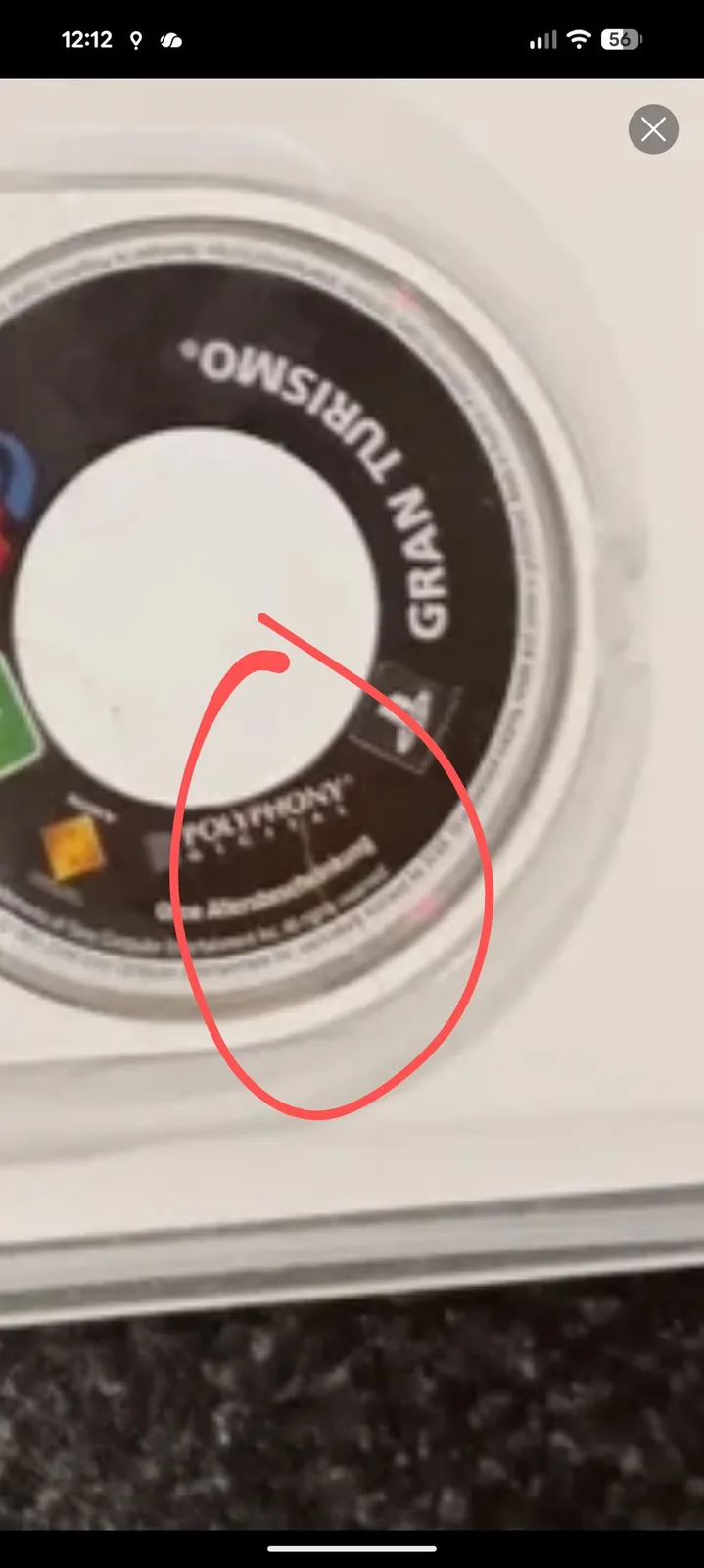 A zoomed phone screenshot of the seller's marketplace listing photo of the Gran Turismo UMD label, with a hand-drawn red circle marking the crack that was already visible in the advert.