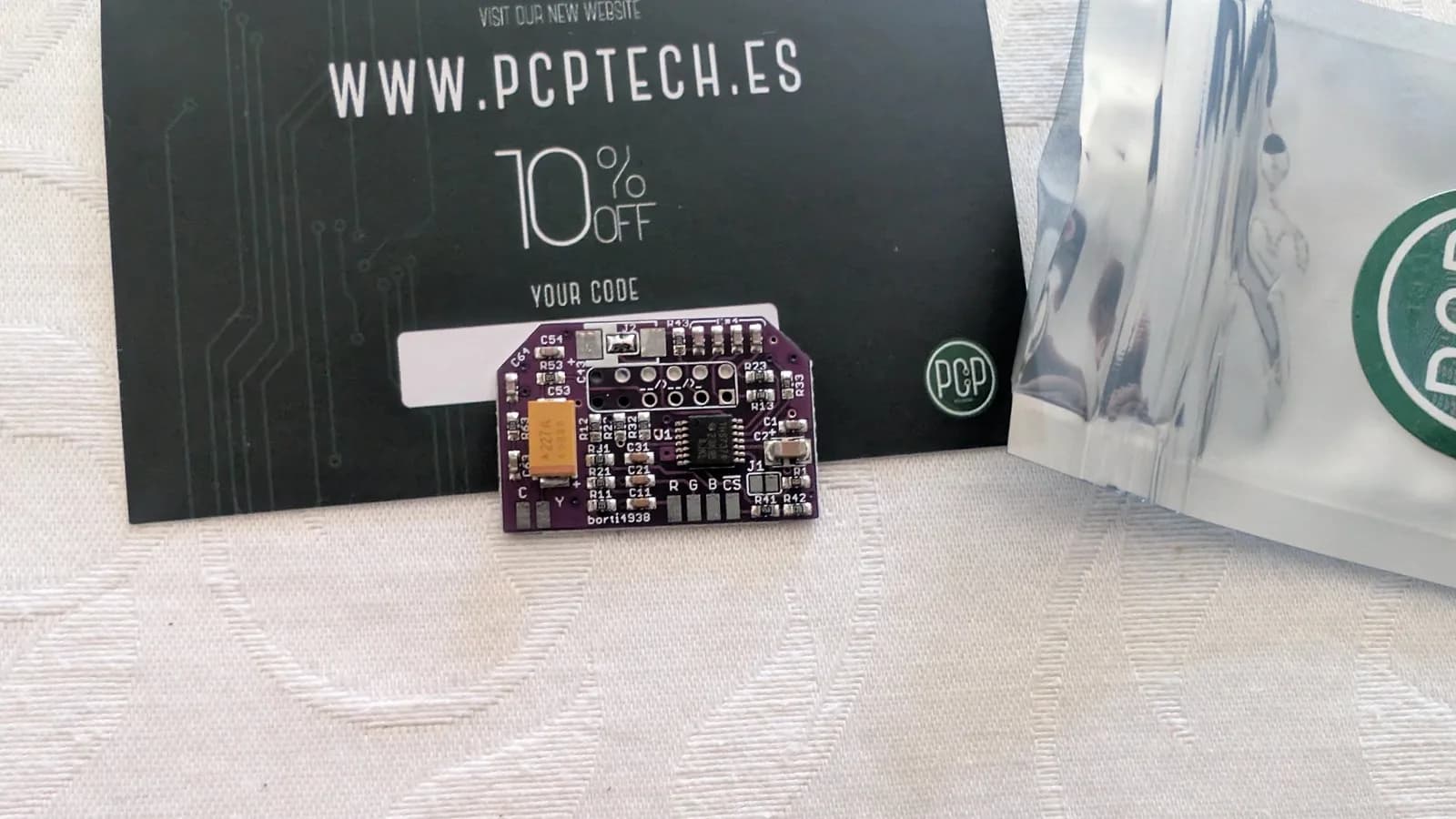 Purple circuit board with yellow capacitor and labeled components next to PCP Tech promotional card with 10% discount code.