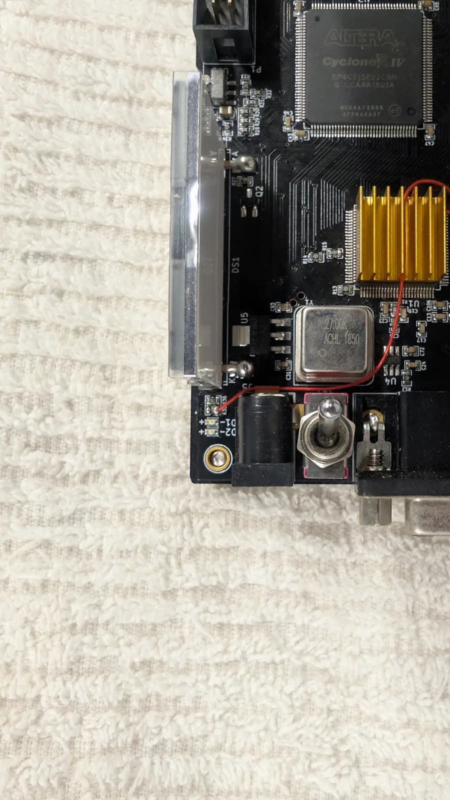 Close-up of the OSSC classic board's top-right: the Altera Cyclone IV FPGA, the gold heatsink, the DC power jack and a toggle switch; the red kynar mod wire runs from a pin of the IC beneath the heatsink, through the heatsink, down to the lower-left of the board.