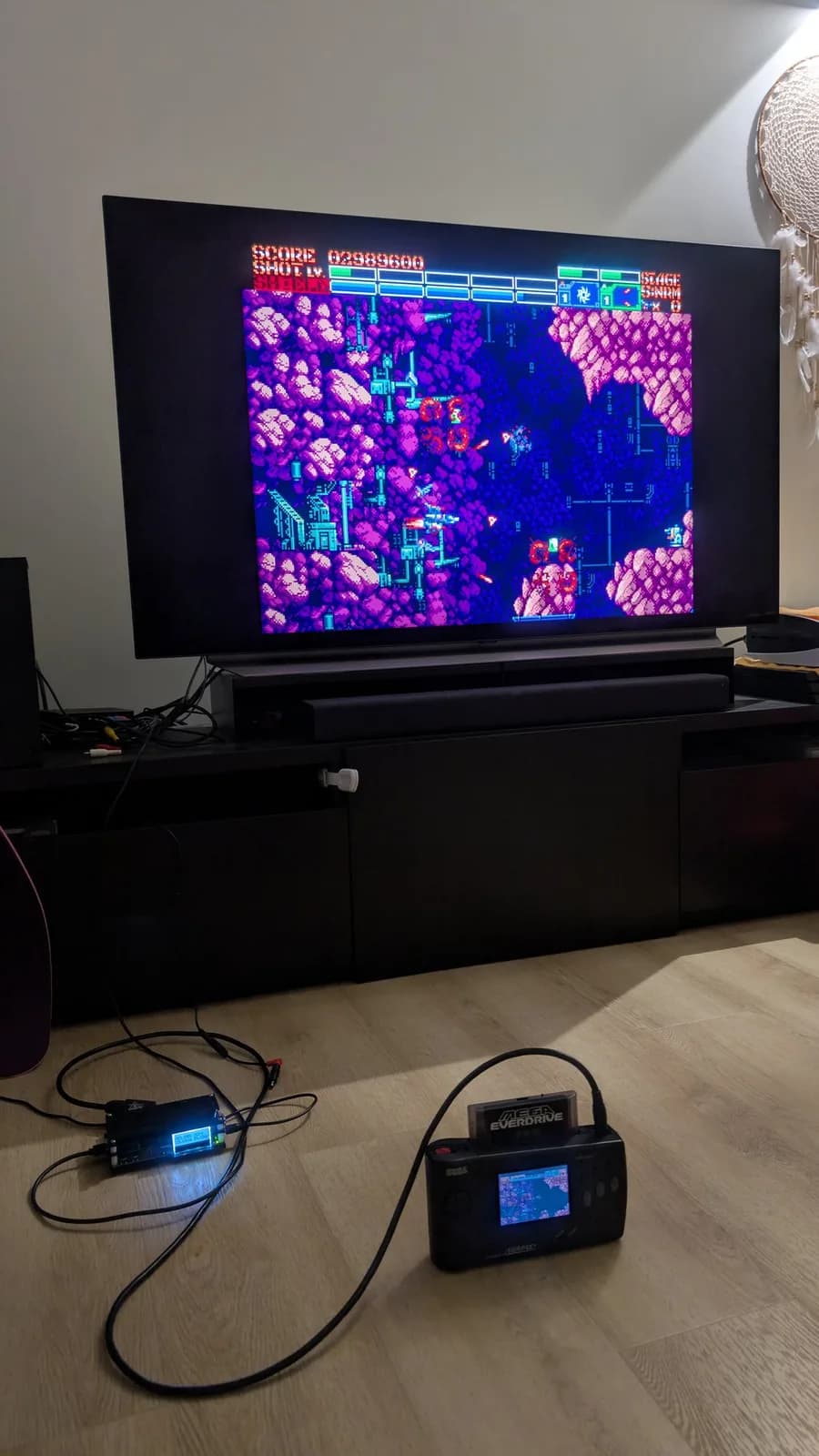 Earthion running in 1440p through the OSSC on a large flat-panel TV; on the floor in front, the OSSC in its case (a small box with a cyan LCD) and a Sega Nomad with a Mega Everdrive Pro cartridge in its slot.