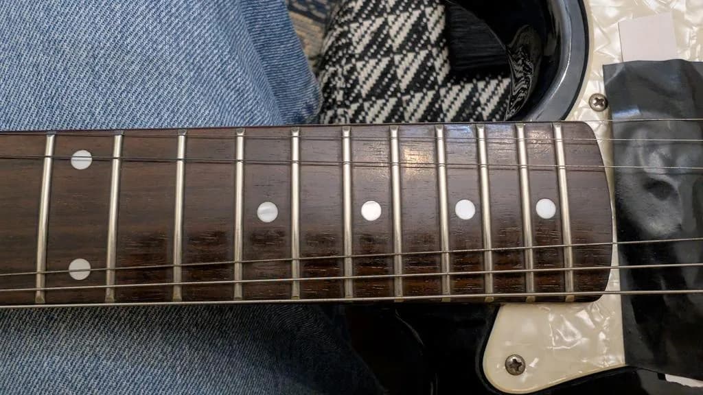 Close-up of electric guitar fretboard showing cleaned rosewood neck with inlaid dot position markers and polished frets.