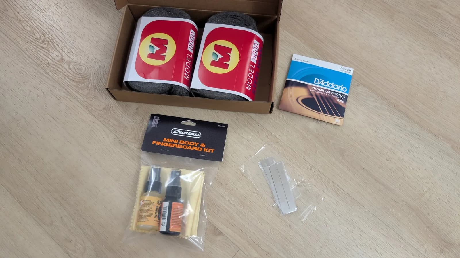 Yamaha FX370C maintenance materials: two red MODEL1000 microfiber cloths, D'Addario strings, Dunlop cleaning kit, and fingerboard/body treatment supplies.