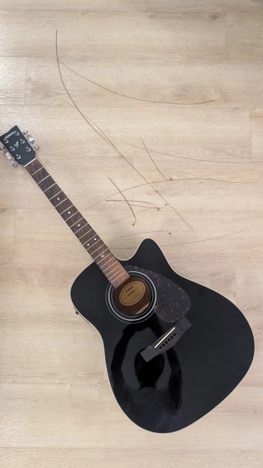 Yamaha FX370C acoustic guitar on light wood floor with removed oxidized strings laid across fretboard during fret cleaning maintenance.