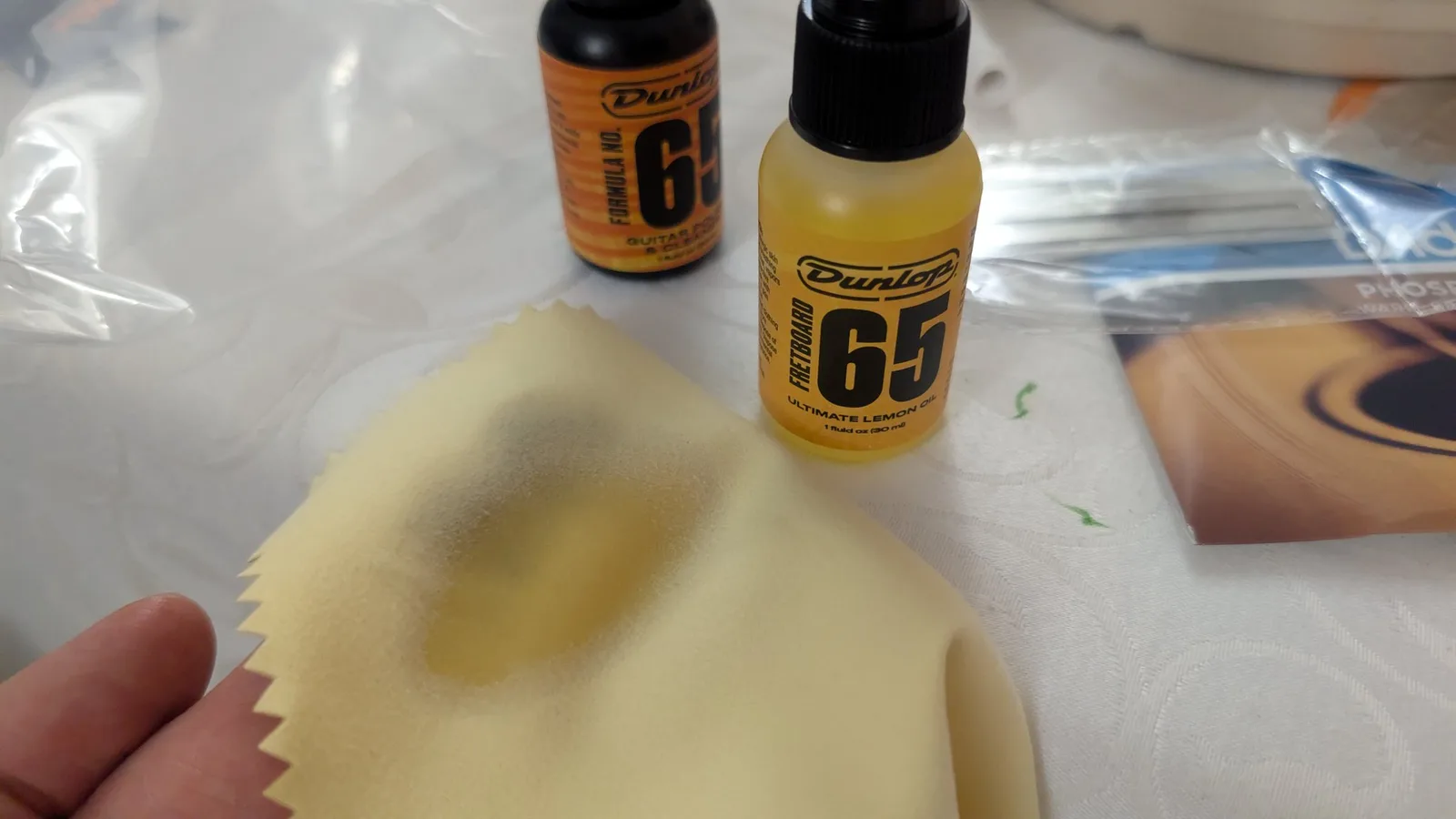 Dunlop Formula 65 lemon oil bottle next to yellow microfiber cloth on workbench during Yamaha FX370C fretboard cleaning.