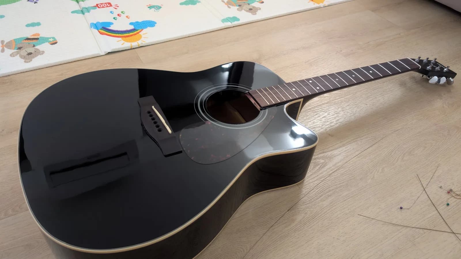 Black Yamaha FX370C acoustic guitar on wooden floor after fret cleaning and fretboard maintenance, showing polished finish.