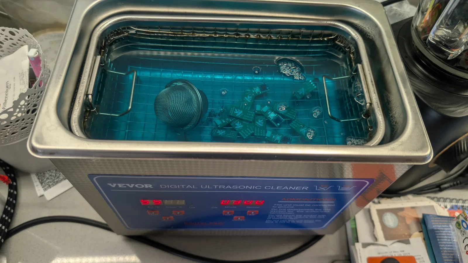 VEVOR digital ultrasonic cleaner, its tank of blue solution holding several fully assembled green WavePhoenix boards (radios reflowed) and a round mesh strainer ball, being cleaned after assembly.