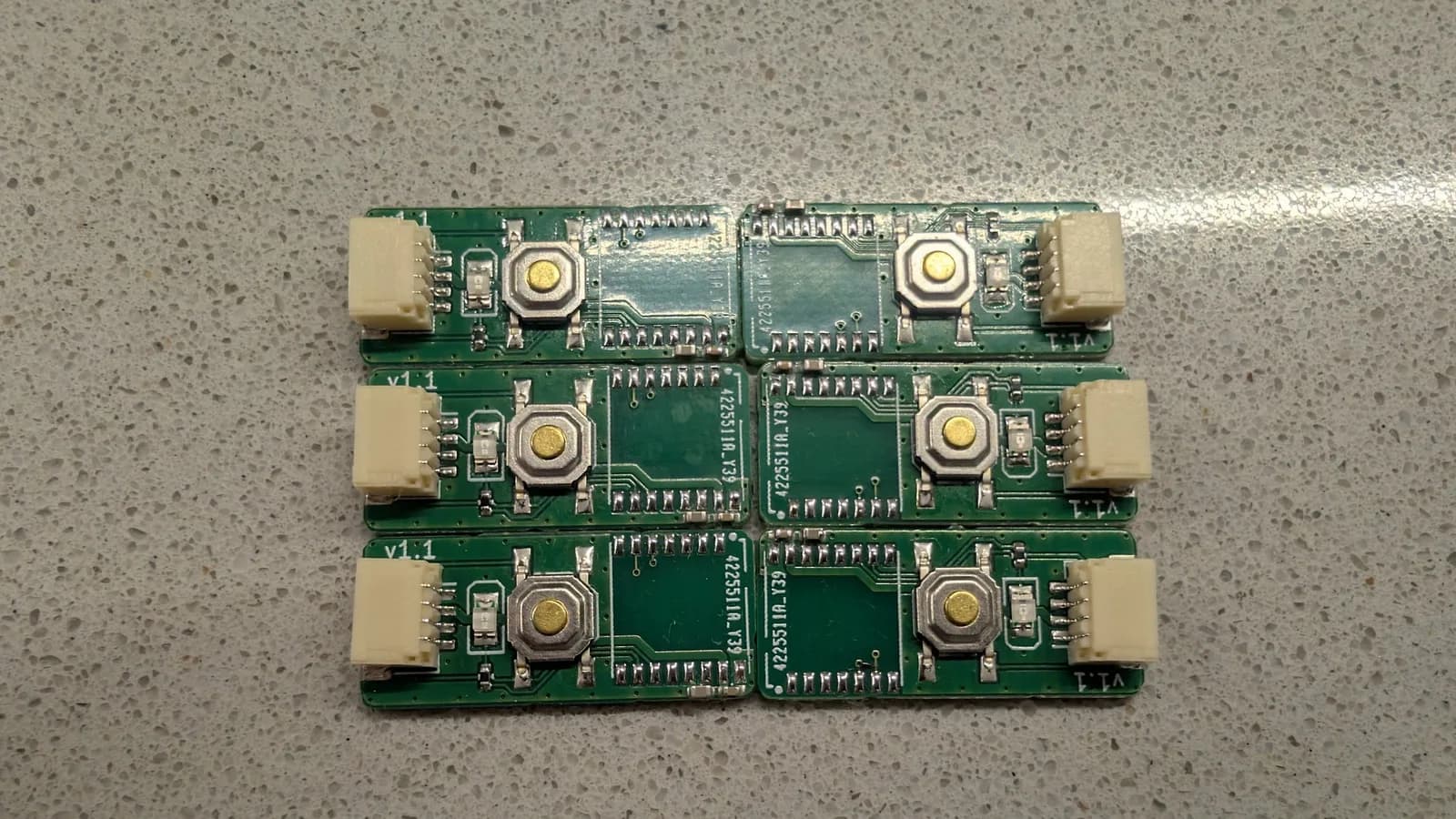 Six green WavePhoenix receiver boards laid edge to edge in a grid on a speckled countertop, each with a pairing button and white JST connector; the radio module is not yet soldered in.