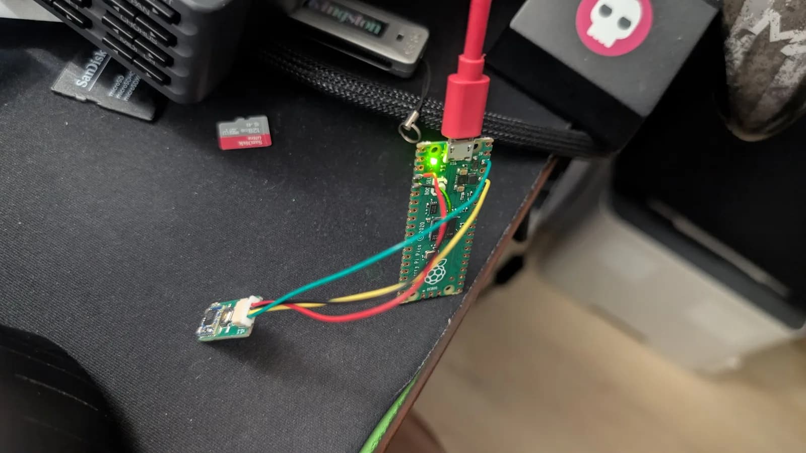 Raspberry Pi Pico debug probe with its green power LED lit, wired to a small WavePhoenix board's JST connector for firmware flashing; USB cable attached.
