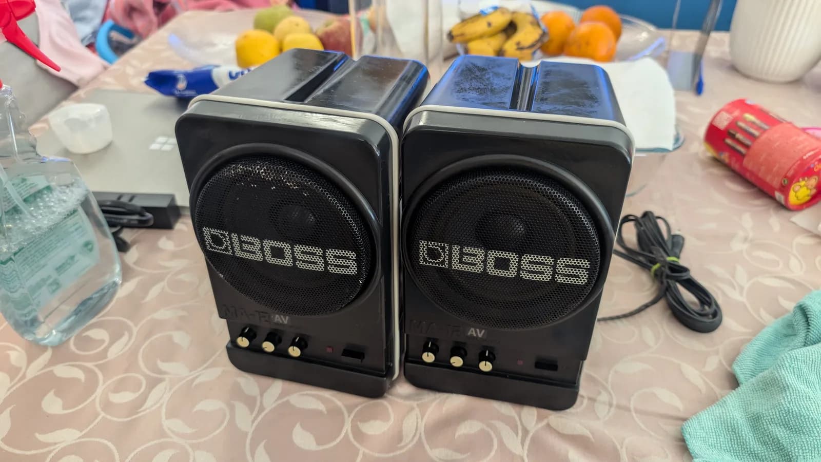 Two refurbished BOSS MA-12AV speakers on a tablecloth, still wet from the Aerospace 303 protectant application, the glossy finish visible on the black cases and grilles.