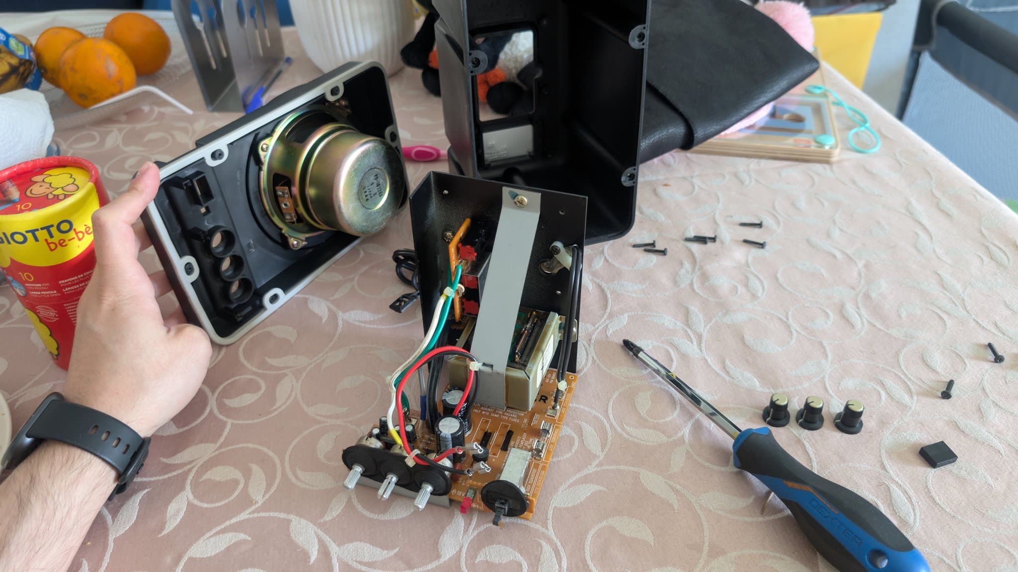 Disassembled BOSS MA-12AV speaker showing driver, PCB with capacitors and wiring, screws, and screwdriver during refurbishment.