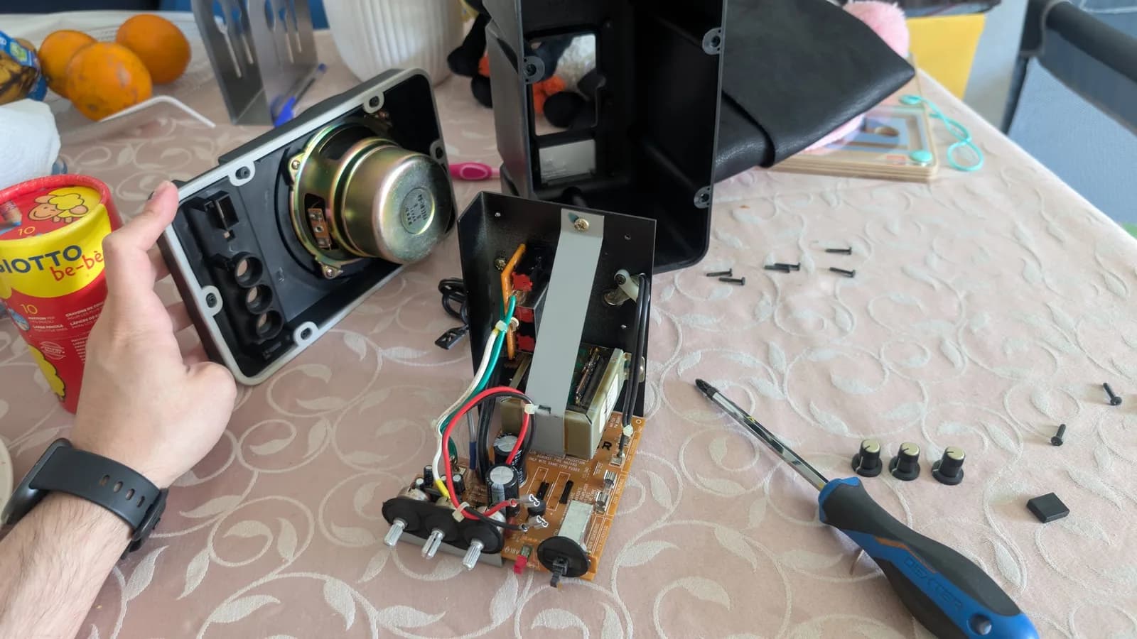 Disassembled BOSS MA-12AV speaker showing driver, PCB with capacitors and wiring, screws, and screwdriver during refurbishment.