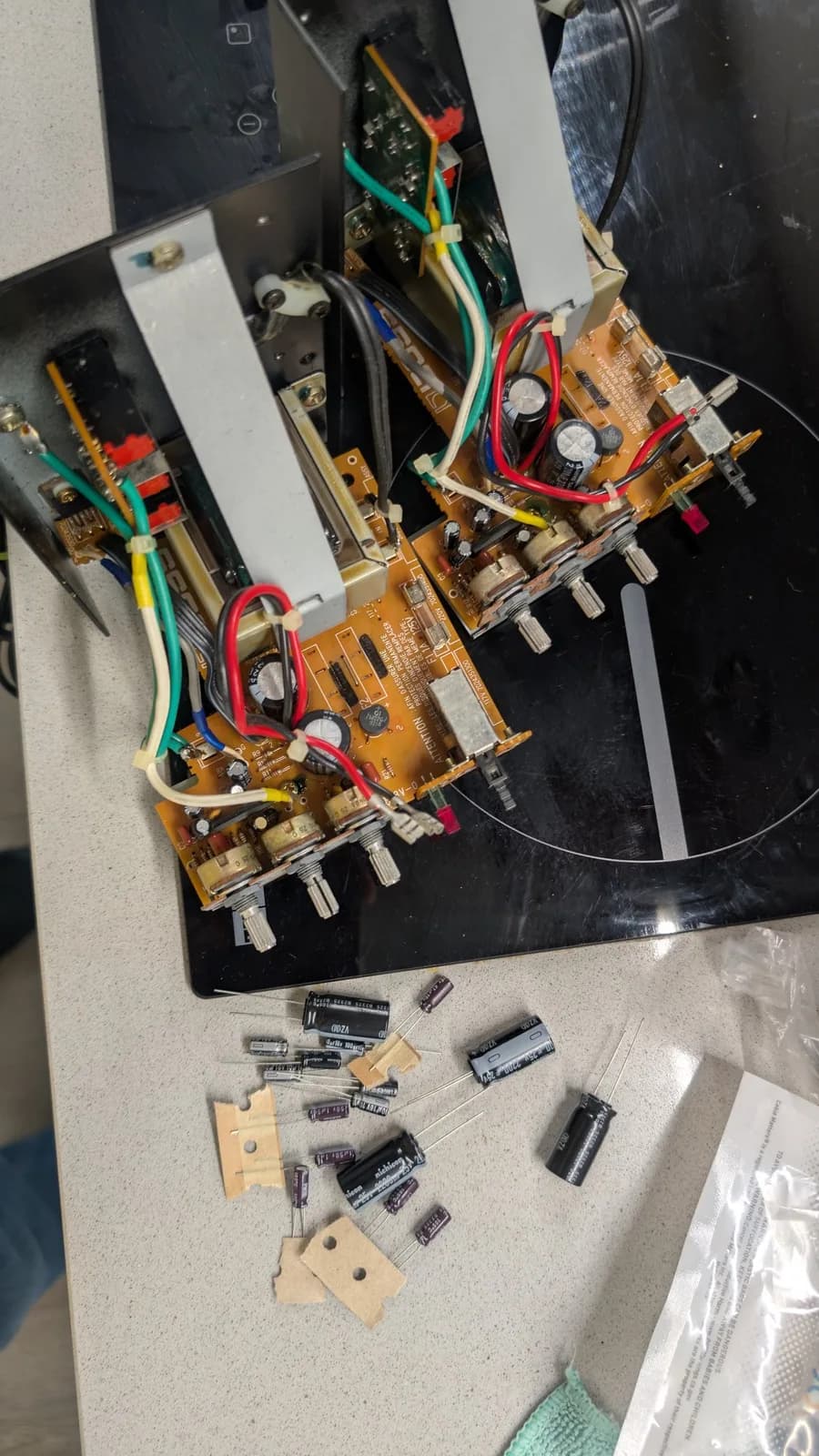 Top view of both BOSS MA-12AV amplifier boards with their old Sanyo electrolytic capacitors still installed and the new Nichicon replacement capacitors laid out in front, ready to be fitted.