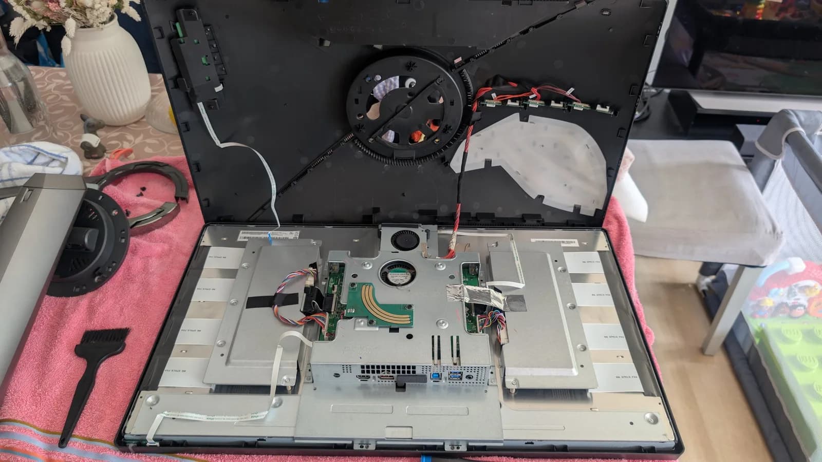 Asus PG27UQ monitor disassembled, exposing mainboard with new capacitors, fan replacement in progress, pink work mat with tools.