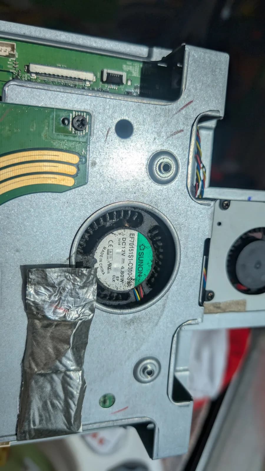 Interior of Asus PG27UQ monitor showing dust-clogged fan with green label, thermal paste residue, and green PCB with ribbon cables visible.